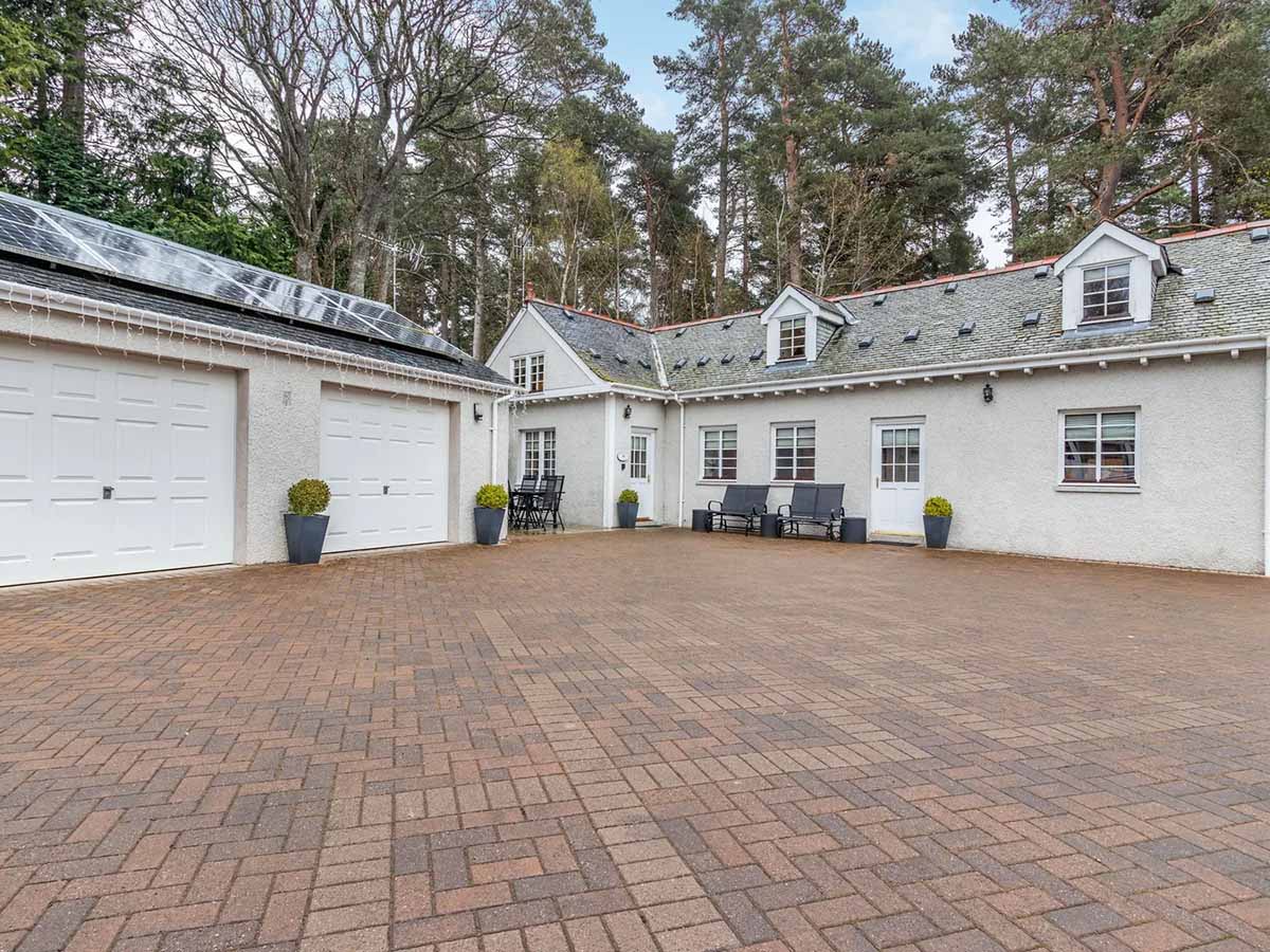 White cottage with red brick driveway and trees in background - Dunstaffnage Cottage