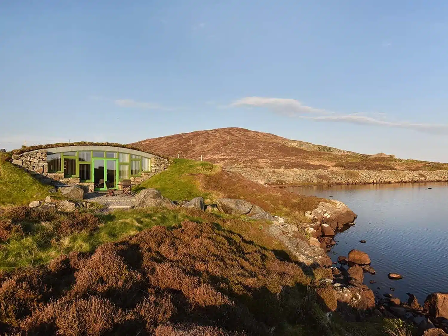 Modern house built into the hillside with glass front overlooking loch Hebridean Earth House South Uist