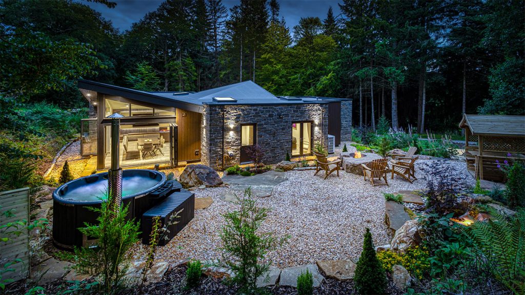 Heilan Roo hot tub in gravel garden surrounded by trees with house in background at night